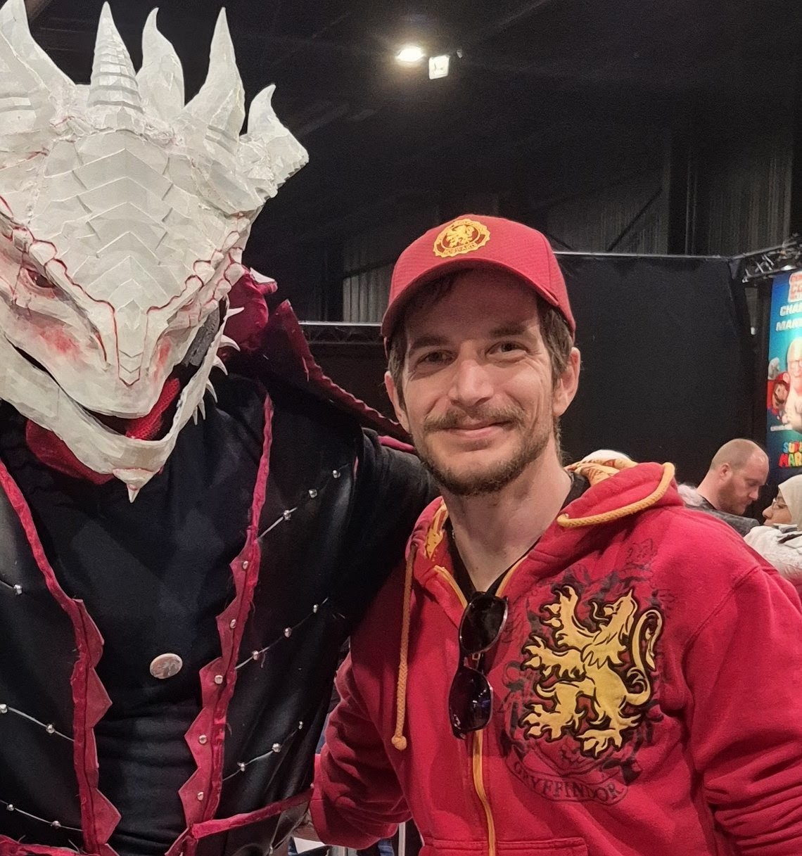 Norbert, wearing a red cap, beside a friend in a full white dragon costume at a convention